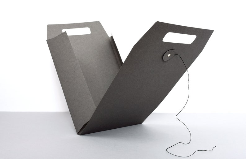 Peut inclure: Une bo&icirc;te en carton noir avec une poign&eacute;e et une fermeture &agrave; cordon. La bo&icirc;te est ouverte et pli&eacute;e en deux.