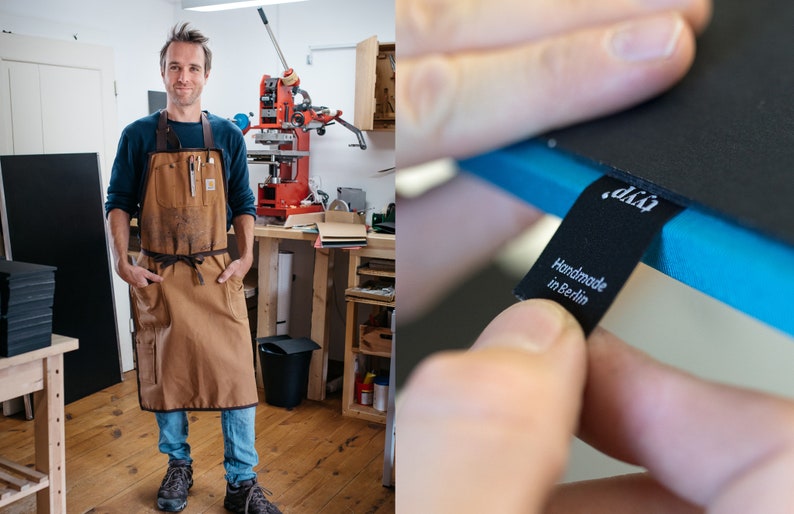 Peut inclure: Un homme portant un tablier en cuir marron se tient dans un atelier avec une presse &agrave; imprimer en arri&egrave;re-plan. Un gros plan sur un carnet en cuir noir avec une bordure bleue et une &eacute;tiquette noire qui indique "d.k.i. Fait main &agrave; Berlin".