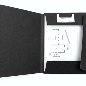 以下が含まれることがあります： 開いた黒いプレゼンテーションフォルダー。家の間取り図と名刺が入っています。間取り図は、部屋にラベルが付けられた詳細な建築図面です。名刺には「HOCH」の文字が印刷されています。