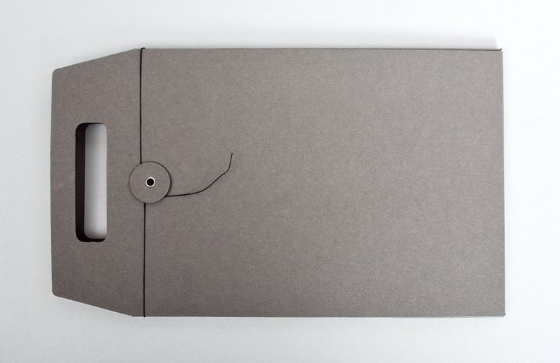 Peut inclure: Une enveloppe en carton gris avec une poign&eacute;e d&eacute;coup&eacute;e et une fermeture &agrave; cordon. L'enveloppe a une surface textur&eacute;e.