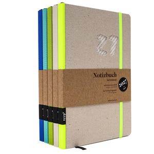 Op de afbeelding: Een stapel van vijf notitieboeken met lichtbruine kaften en neon elastieken. Het bovenste notitieboek heeft het cijfer 27 in reliëf op de kaft en een bruine papieren banderol met de tekst Notizbuch Sketchbook en 2027 erop gedrukt.
