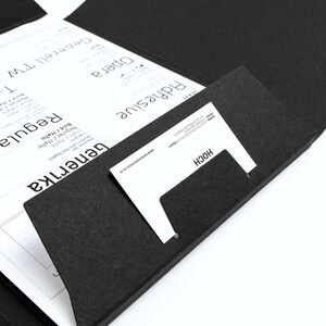 以下が含まれることがあります： 黒いフェルトのドキュメントフォルダー。白い印刷されたシートと名刺が入っています。シートには「Generika」や「T-Star」などのフォント名が表示されています。名刺は白地に黒文字で「HOCH」と書かれています。