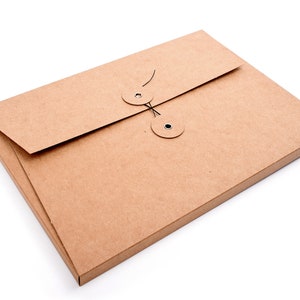 Könnte beinhalten: Ein rechteckiger Dokumentenumschlag aus braunem Kraftpapier mit einem Klappenverschluss, der durch zwei kreisförmige Pappscheiben und eine schwarze Schnur gesichert ist. Der Umschlag hat eine glatte, matte Oberfläche und ein schlichtes Design.