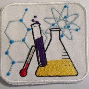 Peut inclure: Un écusson blanc avec une image brodée d'un bécher, d'une éprouvette, d'un thermomètre et d'un atome. Le bécher est rempli de liquide jaune, l'éprouvette est remplie de liquide violet et le thermomètre est rouge. L'atome est bleu et blanc.