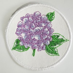 以下が含まれることがあります： 紫色のアジサイの花と緑の葉がついた白い刺繍パッチ