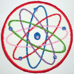 May include: A white fabric patch with a red border, featuring a colorful embroidered atom design. The atom has a blue center with a pink dot, and the orbits are red, green, blue, and purple.