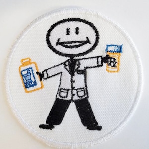 Puede incluir: Parche blanco bordado con un médico de palo que sostiene una botella azul y amarilla en una mano y una botella azul y amarilla en la otra. El médico lleva una bata blanca y una corbata negra. El médico sonríe.