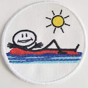 Op de afbeelding: Gestikte patch met een stokfiguur die op een rode opblaasbare vlot in blauw water ligt, met een gele zon erboven.
