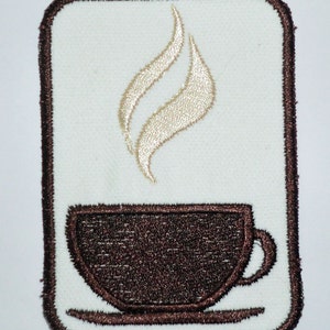 Puede incluir: Un parche bordado marrón con un diseño de taza de café blanca y vapor.