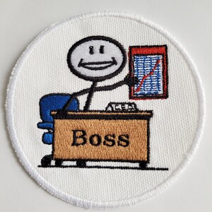 May include: White embroidered patch with a stick figure cartoon of a boss sitting at a desk with a chart. The desk has a brown top and the words "Boss" are embroidered on the front.