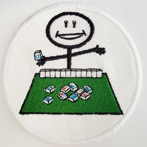 May include: A white embroidered patch with a stick figure holding a tile and sitting at a green mahjong table with white tiles. The stick figure has a smiling face.