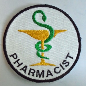 Puede incluir: Un parche bordado blanco con borde negro. El parche presenta un símbolo de caduceo dorado y verde con la palabra "FARMACÉUTICO" escrita alrededor.