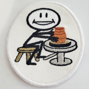 May include: A white embroidered patch featuring a stick figure smiling and using a pottery wheel to shape a brown clay pot.