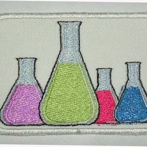 Puede incluir: Cuatro vasos de precipitados de vidrio con líquidos de diferentes colores. Los vasos están dispuestos en una fila de izquierda a derecha. El líquido en el primer vaso es morado, el segundo es verde, el tercero es rosa y el cuarto es azul.