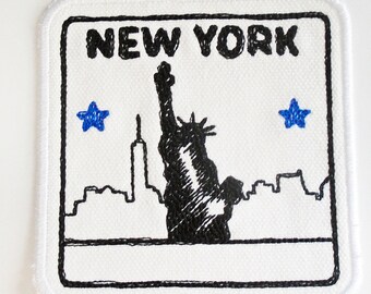 Peut inclure: Patch brodé blanc avec un contour noir. Le patch représente une silhouette noire et blanche de la Statue de la Liberté et de l'horizon de New York. Le texte "NEW YORK" est au-dessus de l'image. Deux étoiles bleues sont de chaque côté de l'image.