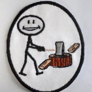 May include: A white embroidered patch with a stick figure holding an axe and chopping wood. The stick figure has a smiling face. The patch is surrounded by a black oval border.