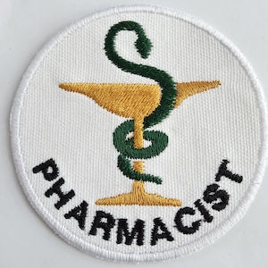 May include: A white, circular embroidered patch featuring a gold mortar and pestle with a green serpent wrapped around it. The word "PHARMACIST" is embroidered in black around the bottom edge of the patch.