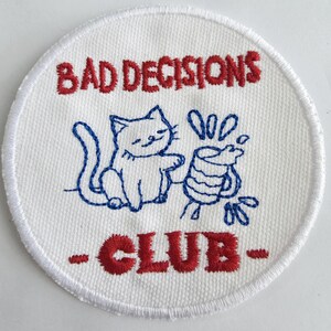 May include: A white ceramic mug with a black handle and the text "But First, Coffee" in a black, handwritten-style font. The mug is on a white surface.