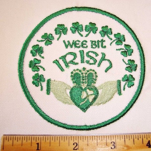 May include: A green embroidered patch with a shamrock design and the text "Wee Bit Irish". The patch features a green heart with a shamrock inside, surrounded by two hands clasped together.