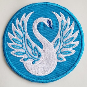 May include: A white swan with outstretched wings embroidered on a round, turquoise blue patch.