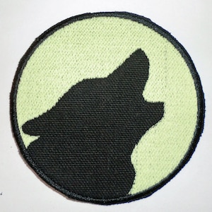 以下が含まれることがあります： 明るい緑色の円形のワッペンに、月に向かって吠える黒い刺繍の狼のシルエットが描かれています。