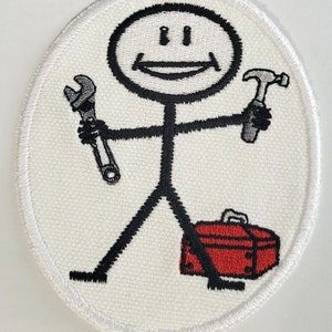 Peut inclure: Un écusson brodé blanc avec un bonhomme bâton tenant une clé à molette et un marteau. Le bonhomme bâton sourit et a une boîte à outils rouge à ses pieds.