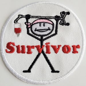 May include: White embroidered patch with a stick figure holding a walking stick and an IV bag. The stick figure is wearing a pink bandana. The text "SURVIVOR" is embroidered in red below the figure.