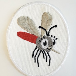 May include: A white oval embroidered patch with a cartoon mosquito. The mosquito has a red proboscis, gray body, black legs, and silver wings.