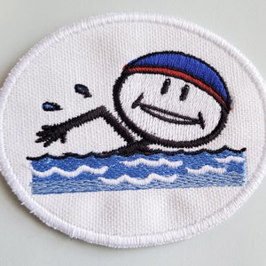 Op de afbeelding: Witte geborduurde patch met een cartoonzwemmer die een blauwe en rode badmuts draagt. De zwemmer glimlacht en heeft zwarte ogen. De zwemmer zwemt in blauw water met witte golven.