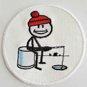 Könnte beinhalten: Runder, gestickter Aufnäher mit einer Strichmännchen-Eisfischerei. Die Figur trägt eine rote Mütze und sitzt auf einem weiß-blauen Eimer. Der Aufnäher hat einen weißen Hintergrund und einen weißen, genähten Rand.
