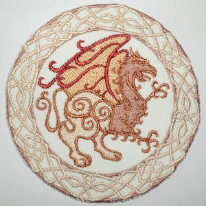 May include: Embroidered patch featuring a winged lion with a Celtic knot border. The lion is depicted in shades of brown and red, with intricate details throughout.