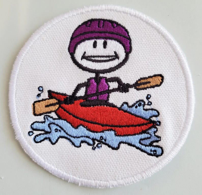 May include: A white embroidered patch featuring a stick figure wearing a purple helmet and a life jacket paddling a red kayak in blue water.