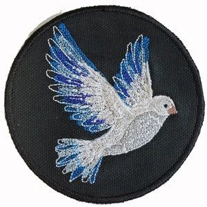 May include: A white dove with blue wings embroidered on a black circular patch.