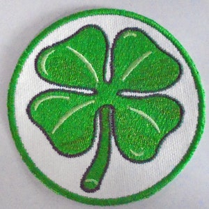 May include: Embroidered patch with a four-leaf clover design in vibrant green. The clover is set within a white circle, edged with a green border. Suitable for application on clothing or accessories.