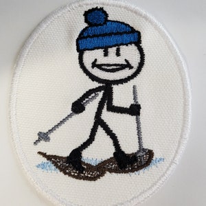 May include: A white embroidered patch with a stick figure wearing a blue hat and snowshoes. The stick figure is smiling and holding two poles.