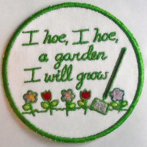 以下が含まれることがあります： 緑色の縁取りのある白い刺繍パッチ。パッチには緑色のクワ、花が咲いた緑色の植物が5つ、そして「I hoe, I hoe, a garden I will grow」というテキストが描かれています。