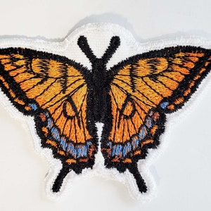 May include: A close-up of an embroidered butterfly patch with orange, black, and blue details. The butterfly is on a white background.