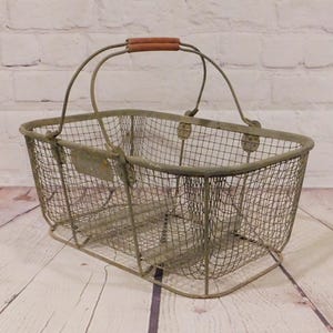 May include: An antique wire mesh basket with a rectangular shape and a curved top. The basket has a metal frame with a distressed, aged appearance. It features a wooden handle and is suitable for storage or display.