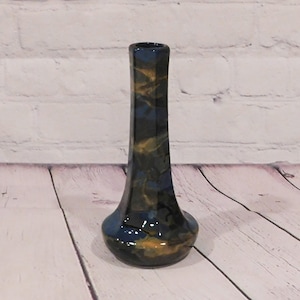 May include: A tall, slender ceramic vase with a flared base and a narrow neck. The surface features a marbled glaze pattern in deep navy blue, black, and metallic gold tones, creating a swirling, fluid aesthetic across the entire exterior.