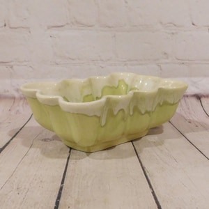 May include: A rectangular ceramic bowl with scalloped edges, featuring a light yellow base color and a creamy white glaze that drips down from the top rim. The bowl has a fluted exterior design and a smooth, glossy finish throughout the piece.