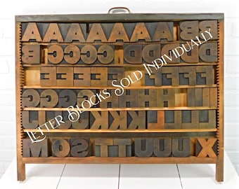 May include: A wooden cabinet with drawers filled with vintage letterpress printing blocks. The cabinet is made of wood and has a dark brown finish. The drawers are labeled with the letters of the alphabet. The text "LETTER BLOCKS SOLD INDIVIDUALLY" is printed on the cabinet.