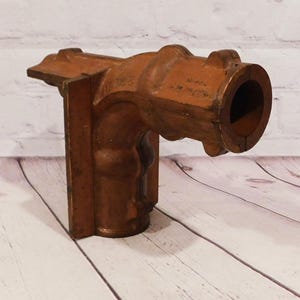 May include: A vintage, wooden architectural element, possibly a decorative bracket or support. The piece is a warm, reddish-brown color with visible wood grain and a weathered appearance. It features a cylindrical opening and a sculpted, curved design.