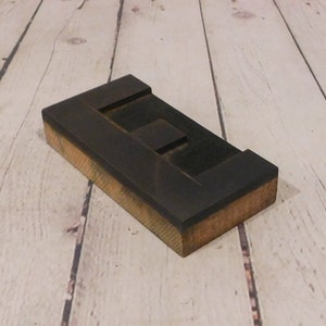 May include: A rectangular wooden block featuring a carved letter E on its top surface. The block has a dark brown finish on the top face and natural light brown wood grain visible along the sides, showcasing a solid construction and block shape.