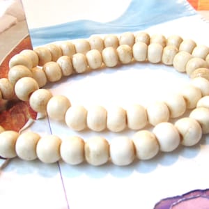 May include: A strand of off-white round beads, made of bone or ivory, strung together with a thin white cord. The beads are slightly irregular in shape and have a matte finish.