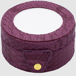 May include: A purple snakeskin jewelry box with a gold button closure and a round, white interior.