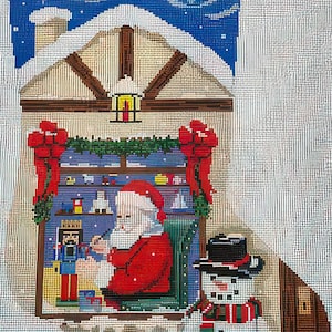 May include: Needlepoint Christmas scene featuring Santa Claus inside a house, with a snowman outside. Santa is seated, wearing a red suit and hat. The house has a snow-covered roof and a window with toys. A snowman with a black hat and scarf is next to the window.