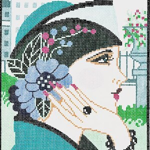 May include: Needlepoint art of a woman in profile, wearing a black hat adorned with pink and blue floral accents. She holds a blue flower, with a black beaded necklace. The background features a cityscape and floral elements.