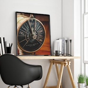 Color photograph of a vintage brass ships telegraph displayed on a simple desk with black chair near a large window.