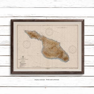 May include: A framed nautical chart of Santa Catalina Island, California, featuring detailed topographical brown shading for the landmass, blue depth soundings, and three compass roses. The map includes printed text and technical data.