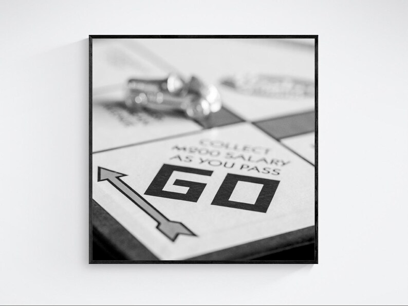 A black and white image of board game. The "GO" space is in focus, with the text "COLLECT $200 SALARY AS YOU PASS" visible. A silver game piece is out of focus in the background.